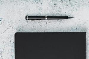 bureau avec bloc-notes noir et stylo sur fond gris. photo