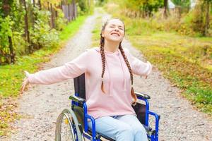 jeune femme handicapée heureuse en fauteuil roulant sur la route dans le parc de l'hôpital en profitant de la liberté. fille paralysée dans une chaise invalide pour personnes handicapées en plein air dans la nature. notion de réhabilitation. photo