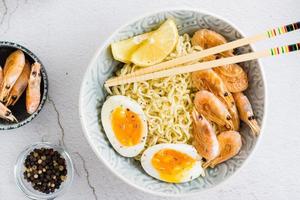 nouilles chinoises aux crevettes frites, œuf à la coque et citron et baguettes dans un bol. vue de dessus photo