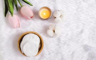 tampons faciaux en coton pour enlever le maquillage avec des fleurs de coton naturel et bougie avec tulipe sur fond de fourrure blanche, hygiène et mode de vie sain photo