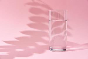 verre d'eau et ombre de feuilles sur fond rose photo