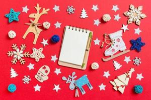 vue de dessus du cahier, des jouets de vacances et des décorations sur fond de noël rouge. concept de temps du nouvel an photo