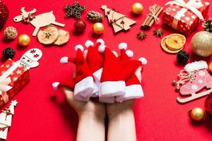 vue de dessus des mains féminines tenant une pile de chapeaux de père noël sur fond rouge. décorations du nouvel an. concept de vacances de noël photo