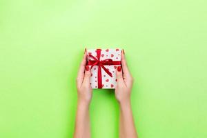 les mains de la femme donnent la saint-valentin enveloppé ou un autre cadeau de vacances fait à la main dans du papier avec un ruban rouge. boîte cadeau, décoration coeur rouge de cadeau sur table verte, vue de dessus avec espace de copie pour votre conception photo