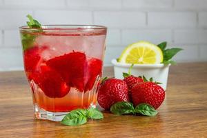 une boisson d'été rafraîchissante avec de la glace, des fraises et du citron sur un fond en bois. le concept de boisson aux fruits. photo