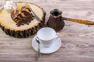 un délicieux gâteau sur une souche en bois avec une tasse à café, une fourchette, une cuillère à thé, des grains de café et un bol avec des morceaux de sucre sur un fond en bois photo