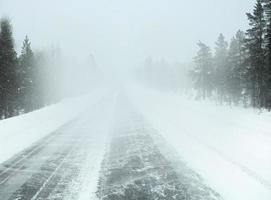 vue en perspective depuis la voiture roulant dans une tempête de neige sur l'autoroute vide en finlande, mauvaise visibilité à travers la vitre du conducteur, forêt couverte de neige au bord de la route, hiver, blizzard photo