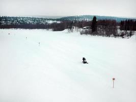 touristes faisant de la motoneige sur glacier à travers les montagnes enneigées en finlande, scène panoramique de collines de neige blanche avec pin. photo