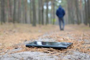 jeune homme perd son smartphone sur le chemin du bois de sapin d'automne russe. négligence et perte d'un concept d'appareil mobile coûteux photo