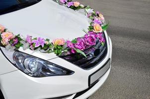 une photo détaillée du capot de la voiture de mariage, décorée de nombreuses fleurs différentes. la voiture est préparée pour une cérémonie de mariage