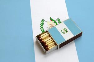 le drapeau du guatemala est affiché dans une boîte d'allumettes ouverte, qui est remplie d'allumettes et repose sur un grand drapeau photo