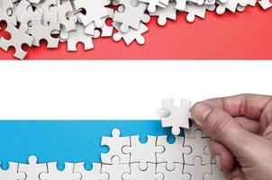 le drapeau luxembourgeois est représenté sur une table sur laquelle la main humaine plie un puzzle de couleur blanche photo