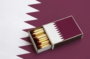 le drapeau du qatar est affiché dans une boîte d'allumettes ouverte, qui est remplie d'allumettes et repose sur un grand drapeau photo