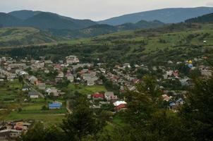 une belle vue sur le village de mezhgorye, région des carpates. beaucoup de bâtiments résidentiels entourés de hautes montagnes forestières et d'une longue rivière photo