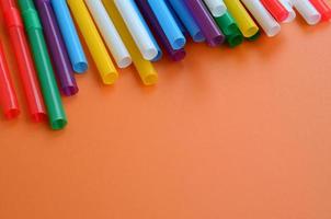 de nombreuses pailles colorées pour les boissons se trouvent sur une surface de fond orange vif photo