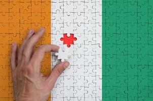 le drapeau de la côte d'ivoire est représenté sur un puzzle, que la main de l'homme complète pour se plier photo