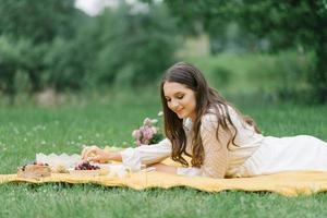 adolescente caucasienne souriante assise à l'extérieur. jeune femme artistique créative portant des vêtements décontractés ayant un pique-nique avec des fruits le jour de l'été. photo