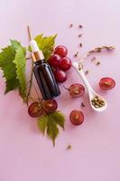 une vue verticale d'une bouteille cosmétique avec une pipette allongée sur une vigne avec des baies rouges et des feuilles. un cosmétique naturel pour les soins de la peau du visage. photo