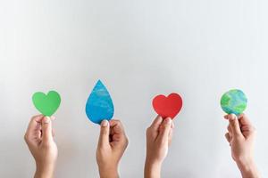 mains tenant la terre, la goutte d'eau, le coeur rouge et la forme de coeur vert. concept de protection du monde contre le réchauffement climatique avec eco-coeur à l'esprit. photo