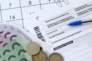 le formulaire fiscal allemand avec un stylo et des factures d'argent européennes se trouve sur le calendrier du bureau. contribuables allemands utilisant l'euro pour payer leurs impôts photo