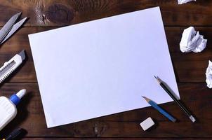 une école ou un bureau nature morte avec une feuille de papier vierge blanche et de nombreuses fournitures de bureau. les fournitures scolaires se trouvent sur un fond en bois marron. place pour le texte photo