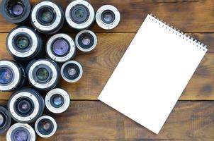 plusieurs objectifs photographiques et un cahier blanc se trouvent sur un fond en bois marron. espace pour le texte photo