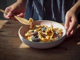 main de femme tenir un plat de pâtes faites maison avec champignons champignons et sauce carbonara. photo
