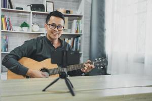 professeur de musique asiatique homme diffusant des cours de guitare en direct aux étudiants en ligne à l'aide de mobile. musicien masculin asiatique jouant de la guitare en chantant des vidéoconférences en direct à la maison. musique de concert en direct de n'importe où. photo