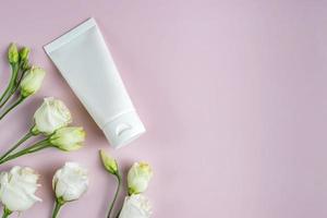 crème hydratante pour les mains maquette de tube en plastique blanc sur fond rose trandy avec fleurs d'eustoma. emballage de produit de beauté vierge pour les soins de la peau photo