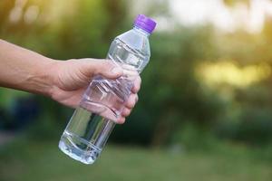 la main en gros plan tient une bouteille d'eau potable avec un capuchon violet. concept boire de l'eau pour la santé, rafraîchir le corps, soulager la soif. photo