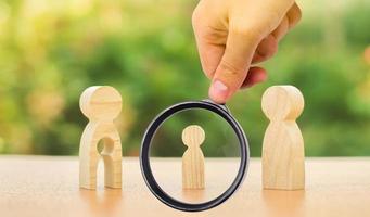 une loupe regarde une figure d'enfant se tient entre le père et la mère. l'enfant choisit avec quel parent vivre après son divorce. tutelle sur l'enfant. intérêt de l'enfant photo