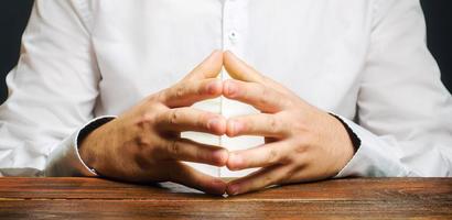 un homme est assis à une table avec ses mains dans la serrure. la résolution des conflits et la recherche d'un compromis. réfléchir à un problème et trouver un consensus. penser à la tâche. calme et professionnalisme photo