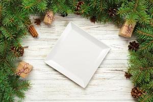 vue de dessus. assiette carrée blanche vide sur fond de noël en bois. concept de plat de dîner de vacances avec un décor de nouvel an photo