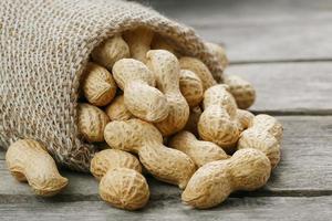 cacahuètes dans un sac de toile de jute miniature sur une vieille surface en bois grise photo