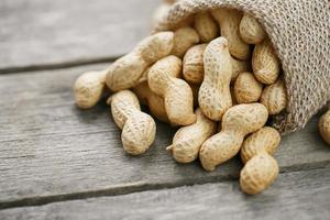 cacahuètes dans un sac de toile de jute miniature sur une vieille surface en bois grise photo