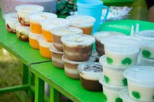 des puddings dans des récipients en plastique sont placés sur une table verte, vendus par des marchands ambulants photo