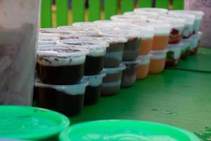 des puddings dans des récipients en plastique sont placés sur une table verte, vendus par des marchands ambulants photo