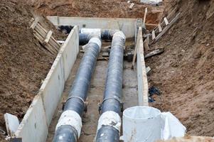 grandes conduites d'eau en métal noir et en plastique pour l'eau chaude et froide sur un chantier de construction lors d'une réparation dans un nouveau quartier sous terre photo