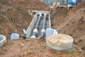 grandes conduites d'eau en métal noir et en plastique pour l'eau chaude et froide sur un chantier de construction lors d'une réparation dans un nouveau quartier sous terre photo