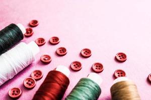 belle texture avec beaucoup de boutons rouges ronds pour la couture, la couture et les écheveaux de bobines de fil. espace de copie. mise à plat. fond rose, violet photo