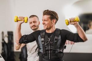 homme faisant de l'entraînement ems avec entraîneur dans la salle de sport photo