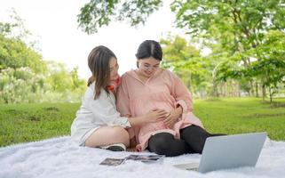 famille lesbienne heureuse femme enceinte se détendre dans le parc. les homosexuels ont une relation affectueuse comme un couple marié. personne homosexuelle a l'égalité d'être parent. mode de vie maternité grossesse lgbtq. photo