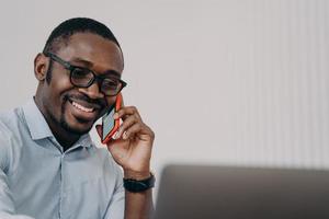 un homme d'affaires afro-américain souriant répond à un appel d'affaires téléphonique sur un ordinateur portable, parle, consulte un client photo