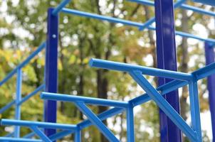 tuyaux métalliques bleus et barres transversales contre un terrain de sport de rue pour l'entraînement en athlétisme. équipement de gym athlétique en plein air. photo macro avec mise au point sélective et arrière-plan extrêmement flou