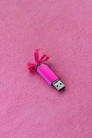 carte mémoire flash usb rose brillante avec un arc rose se trouve sur une couverture en tissu polaire rose clair doux et poilu. conception de cadeau féminin classique pour une carte mémoire photo
