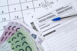 le formulaire fiscal allemand avec un stylo et des factures d'argent européennes se trouve sur le calendrier du bureau. contribuables allemands utilisant l'euro pour payer leurs impôts photo