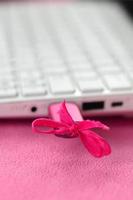 une clé USB rose brillante avec un arc rose est connectée à un ordinateur portable blanc, qui repose sur une couverture en tissu polaire rose clair doux et moelleux. design féminin classique pour une carte mémoire photo