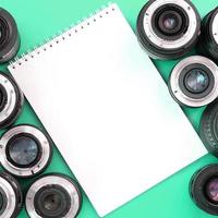 plusieurs objectifs photographiques et un cahier blanc reposent sur un fond turquoise vif. copie espace photo