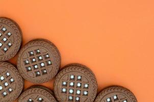 image détaillée de biscuits sandwich ronds brun foncé fourrés à la noix de coco sur une surface orange. image de fond d'un gros plan de plusieurs friandises pour le thé photo