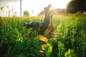 femme et homme s'amusant à l'extérieur. couple de hipster aimant marchant dans le champ, s'embrassant et se tenant la main, se serrant dans ses bras, allongé dans l'herbe et levant les jambes en été au coucher du soleil. La Saint-Valentin photo